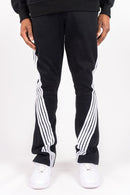Black track pants with white diagonal stripes down the sides, worn by a model with white sneakers against a plain white background. By Fresh N Fitted 