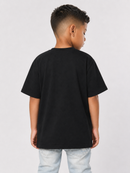 A child model shown from the back wearing a plain black short-sleeve t-shirt and light wash jeans, photographed against a neutral light gray studio background.