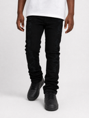 A person wearing black distressed skinny jeans with tonal embroidery down the legs, styled with a white t-shirt and black sneakers against a light gray studio background.