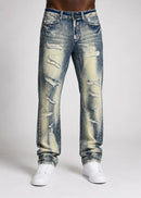 Distressed blue denim jeans with heavy fading and ripped details, shown on a model from the waist down wearing white sneakers against a light gray studio background. By Fresh N Fitted.