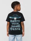 A child model shown from the back wearing a black t-shirt with a graphic of a blue flying saucer and the text 'REACH YOUR INNER PEACE' in a stylized light blue font, paired with light blue jeans against a light gray background.