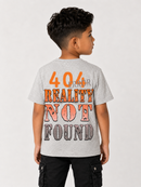 A child model shown from the back wearing a light heather gray t-shirt with a humorous graphic that reads '404 REALITY NOT FOUND' in orange and gray text, paired with black cargo pants against a plain light gray background.