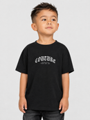 A young boy wearing a black short-sleeve t-shirt with a white gothic-style 'COUTURE' graphic on the chest, paired with dark gray jeans, photographed against a solid light gray background.