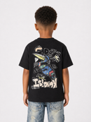 A child viewed from behind wearing a black short-sleeve graphic T-shirt and light blue jeans against a plain light gray studio background.