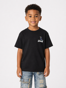A young boy wearing a black short-sleeve t-shirt with a small white and blue graphic on the left chest, paired with distressed blue jeans, standing against a light gray background.