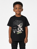A young boy wearing a black graphic t-shirt with a cartoon dog design and the text 'STAY BUST EVERYTHING OMG!', paired with black distressed jeans, against a light gray background.