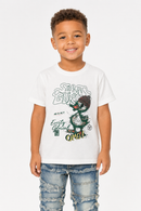 A young boy smiling and wearing a white graphic t-shirt with a green cartoon character and the words 'Everything Omg!' printed on the front, paired with distressed blue jeans, against a plain white background.