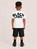 A child model shown from the back wearing a white t-shirt with a large black 'BLACK LABEL' graphic on the back, paired with black shorts, socks, and sneakers, against a light textured beige background.