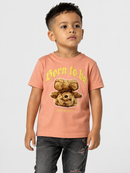 A young boy wearing a peach-colored graphic t-shirt with a teddy bear design and the text 'Born to be Different', paired with dark gray jeans, standing against a light gray background.
