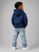 A child model shown from the back wearing a navy blue hoodie, light wash blue jeans, and white sneakers against a solid gray studio background.