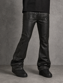 Black leather flare jeans with tonal gothic-style embroidery on the upper thighs, shown on a model from the waist down against a textured gray studio background.