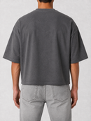 A man viewed from the back wearing a dark gray cropped t-shirt and light gray jeans, set against a neutral light gray background.