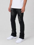 A person wearing black jeans with silver rhinestone star patterns on the thighs, styled with a white t-shirt and white sneakers against a light gray studio background.
