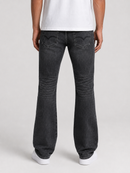 Rear view of a person wearing dark gray flared jeans, a white t-shirt, and white sneakers against a light gray studio background.