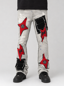 A pair of light-wash distressed denim jeans with ripped details and large red and black patchwork embellishments, shown on a model from the waist down against a light gray background.