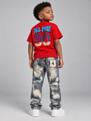 A young boy is shown from the back wearing a red t-shirt with 'ALL PRO 00' printed in blue and gold, paired with distressed blue jeans and white sneakers, against a solid gray studio background.