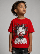 A young boy with dreadlocks wearing a bright red graphic t-shirt featuring a stylized clown face with headphones and a red pacifier, paired with distressed black jeans, against a solid gray studio background.