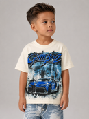A young boy wearing a cream-colored t-shirt with a blue and black 'Gatbooz' graphic featuring a sports car, paired with light-wash blue jeans, set against a plain gray studio background.