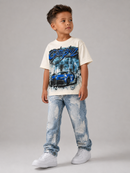 A young boy modeling a cream-colored t-shirt with a blue and black 'Gangster' graphic print featuring a sports car, paired with distressed light blue jeans and white sneakers, against a solid gray studio background.