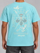 A man wearing a light blue t-shirt, showing the back of the shirt with a detailed white graphic print featuring a double-decker bus, birds, swords, and the text 'ABOUT ALL THINGS' and 'GOTTY UND'. By Fresh N Fitted