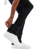 A close-up of a person's legs wearing black pants and white low-top sneakers, with one hand adjusting the cuff of the pants against a plain white background.