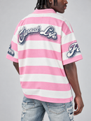A man wearing a pink and white striped short-sleeve shirt with 'Eternal Life' written across the back in a stylized silver and black script, paired with distressed blue jeans against a light gray studio background.
