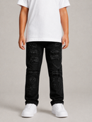 A child wearing black distressed jeans with ripped details, a white t-shirt, and white sneakers, standing against a neutral gray studio background.