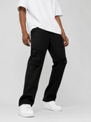 A model wearing black distressed jeans with ripped details on the thighs and knees, styled with a white t-shirt and white sneakers against a light gray studio background.