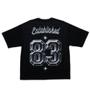 A black short-sleeve t-shirt shown from the back, featuring a large graphic print with the word 'Established' in white cursive script above the number '83' in a 3D metallic silver block font with white star accents. By Fresh N Fitted.