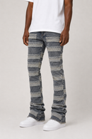 A person wearing distressed gray denim jeans with horizontal patchwork-style striping and frayed hems, styled with a white t-shirt and white sneakers against a light gray studio background.