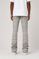 Rear view of a person wearing light gray pleated denim jeans, a white t-shirt, and white sneakers against a light gray studio background.