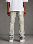 Rear view of a person wearing light-wash blue and cream marbled denim jeans with a white t-shirt and white sneakers, standing against a textured gray studio wall.