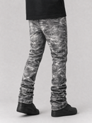 A person shown from the waist down wearing gray and black acid-washed denim jeans with a scrunchie ankle fit, paired with black sneakers and a black t-shirt, against a light gray studio background.