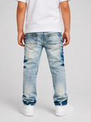 A child shown from the back wearing light-wash blue denim jeans with a faded wash, a white t-shirt, and white sneakers against a light gray studio background.