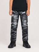 A child wearing black and white distressed denim jeans with ripped details and white patches, paired with a black t-shirt and black sneakers, shown against a light gray studio background.