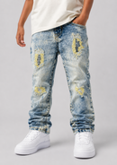 A person wearing light-wash blue distressed jeans with ripped details and yellow-toned patch accents, paired with a white t-shirt and white sneakers, shown from the waist down on a light gray studio background.