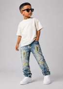 A young boy modeling a casual outfit consisting of a white t-shirt, distressed blue jeans with yellow patches, and white sneakers, while wearing black sunglasses against a solid gray background.