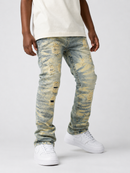 A person wearing distressed light blue denim jeans with yellow-tan faded wash patches, paired with a cream t-shirt and white sneakers, shown from the waist down on a light gray studio background.