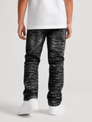 A child wearing black acid-wash slim-fit jeans with a distressed, marbled texture, styled with a white t-shirt and white sneakers against a light gray studio background.