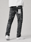 A person shown from the waist down wearing slim-fit black acid-wash jeans with white sneakers and a white t-shirt, photographed against a light gray studio background.