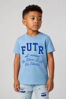 A young boy wearing a light blue t-shirt with 'FUTR' and 'The Future Is Us' printed in dark blue on the front, paired with distressed light blue jeans, photographed against a neutral gray background.