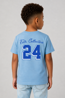 A child model shown from the back wearing a light blue t-shirt with 'Futr Collective' and the number '24' printed in blue and white on the back, paired with light blue jeans against a neutral gray background.