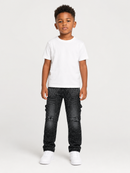 A young boy modeling a white crewneck t-shirt and dark distressed cargo jeans with white sneakers, standing against a light gray studio background.