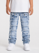 A child wearing light blue heavily distressed ripped jeans with frayed edges and patch pockets, styled with a white t-shirt and white sneakers against a light gray studio background.
