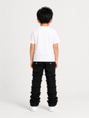 A child model shown from the back wearing a white short-sleeve t-shirt and black distressed denim jeans with stacked ruffle details down the legs, set against a plain light gray studio background.