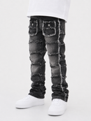 A pair of distressed black denim jeans with unique patchwork paneling and frayed details, styled with a white t-shirt and white sneakers on a light gray background.