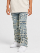 A person wearing light-wash distressed denim jeans with diagonal frayed striping and ruffled detailing, paired with white sneakers and a light beige top, shown against a plain light gray studio background.