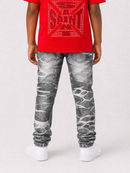 A child shown from the back wearing a bright red t-shirt with a large red 'SAINT' graphic and distressed gray jeans with a white marble pattern, paired with white sneakers, against a light gray background.