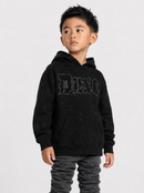A young boy wearing a black distressed hoodie with a rhinestone-embellished 'DIAN' logo on the chest, paired with dark gray ruched pants, photographed against a light gray studio background.
