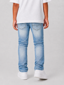 A child wearing light wash blue denim jeans, a white t-shirt, and white sneakers, shown from the back against a light gray studio background.